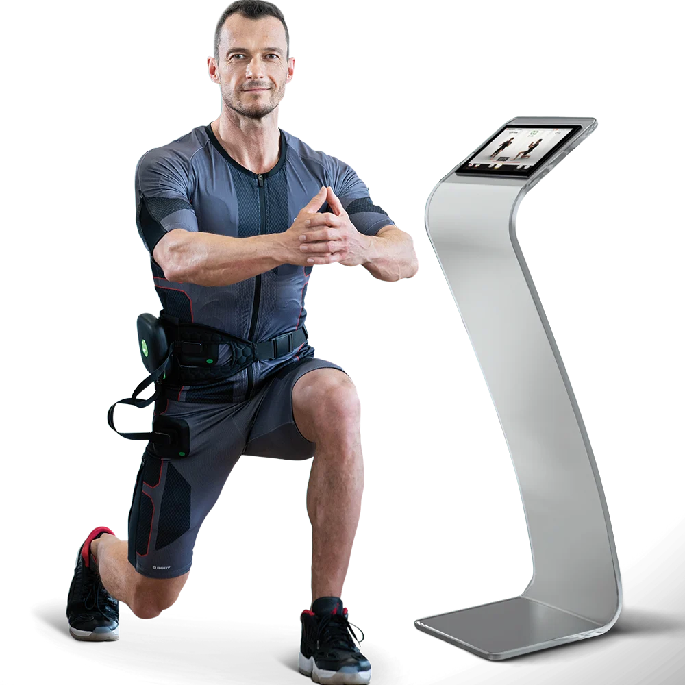 XBody Ein Mann in Sportkleidung macht neben einem Fitnessgerät mit Bildschirm einen Ausfallschritt.