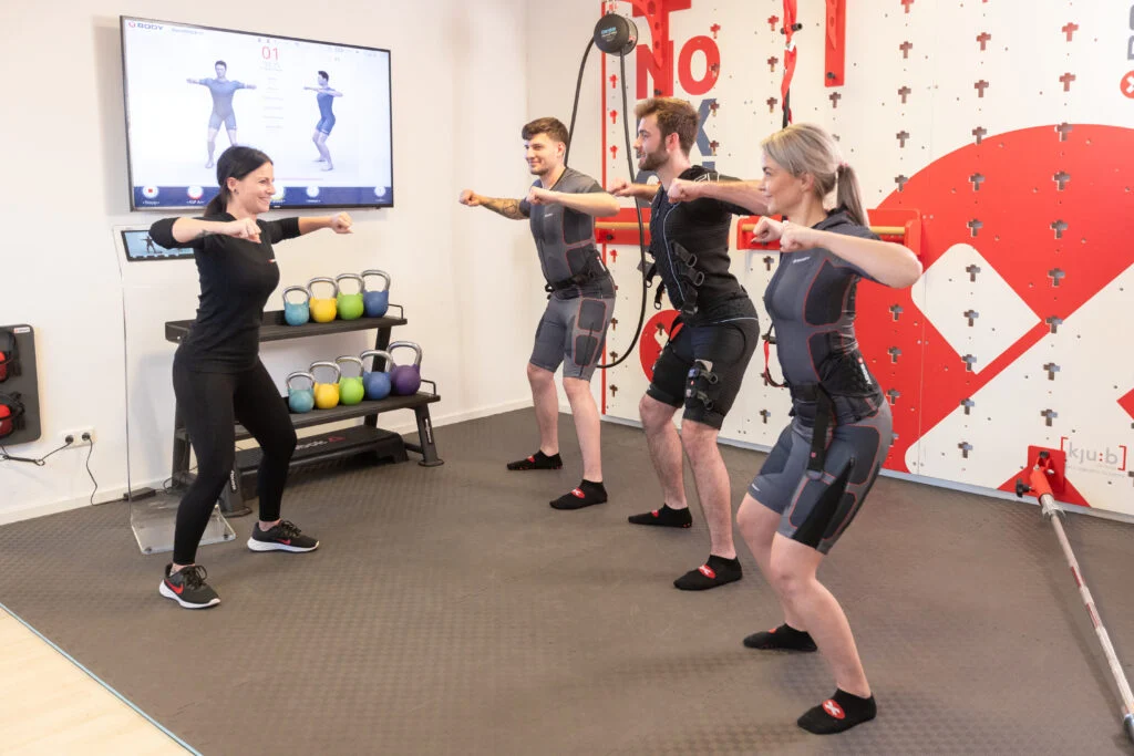 XBody Vier Personen in Sportkleidung machen zusammen mit einem Trainer in einem Fitnessstudio Kniebeugen.