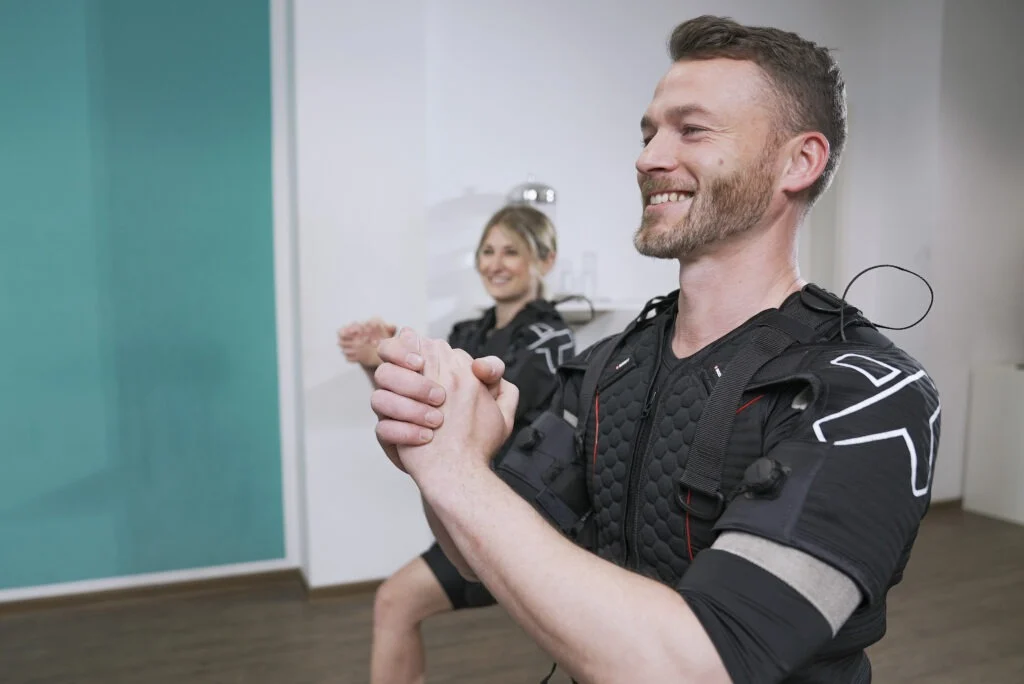 XBody Zwei Menschen, die lächeln und trainieren, während sie EMS-Anzüge (Elektrische Muskelstimulation) tragen. XBody Zwei Menschen, die lächeln und trainieren, während sie EMS-Anzüge (Elektrische Muskelstimulation) tragen.