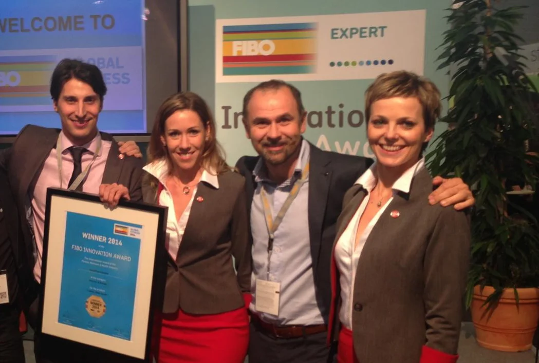 Bild Fibo Award 2014 XBody Vier Personen in Geschäftskleidung lächeln mit einer Auszeichnungstafel bei einer FIBO-Innovationsveranstaltung.