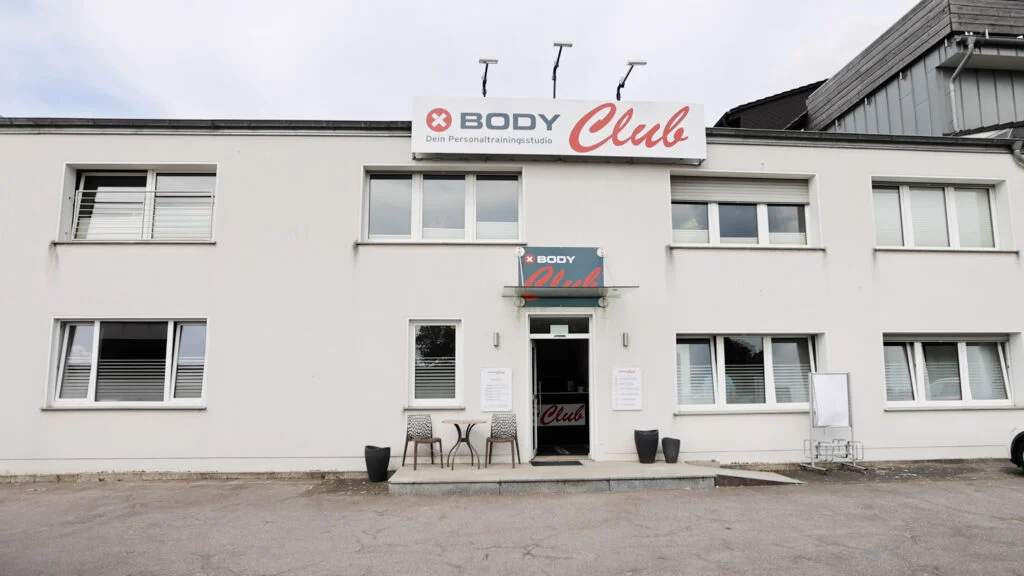 IMGL6455-1024x576 XBody Weißes Gebäude mit einem „BODY Club“-Schild über dem Eingang, Terrassenstühle neben der Tür.
